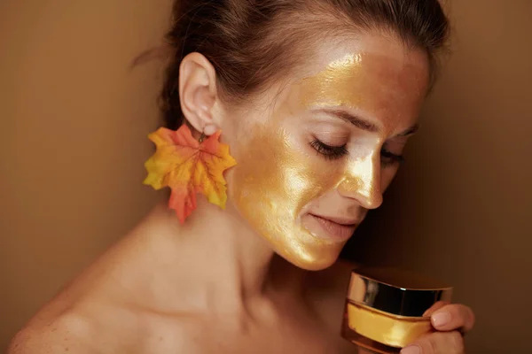 Vrouw met gouden masker houden crème tegen bronzen achtergrond — Stockfoto