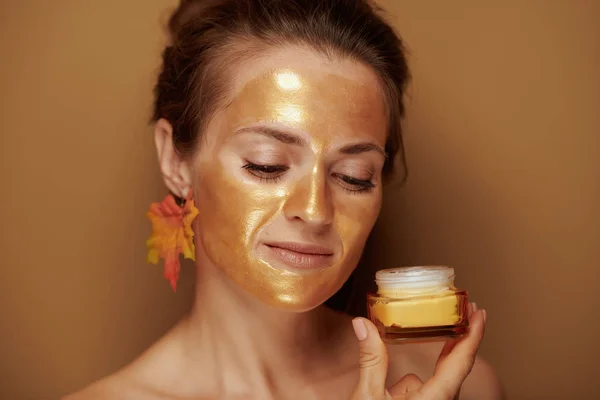 Ibu rumah tangga muda dengan topeng emas menggunakan produk kosmetik — Stok Foto