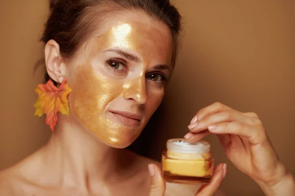 Jonge vrouw met gouden masker met behulp van cosmetische product — Stockfoto