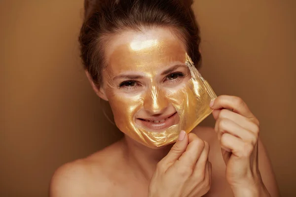 Glimlachende vrouw verwijderen gouden masker tegen bronzen achtergrond — Stockfoto