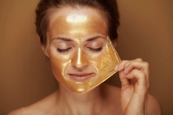 ベージュの背景に金色のマスクを削除する現代女性 — ストック写真