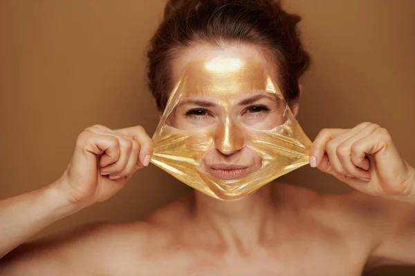 Kobieta usuwając złotą maskę izolowane na brązowym tle — Zdjęcie stockowe