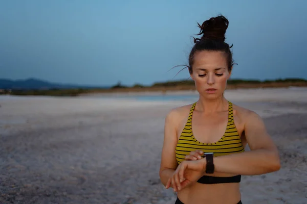 fitness sports woman in sport style clothes on the beach in the evening using smart watch to track weight in fitness app.