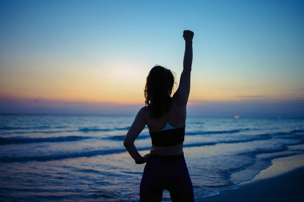 夕方には海岸で腕を開いて海を楽しむスポーツスタイルの服で健康なスポーツの女性の後ろから見た — ストック写真