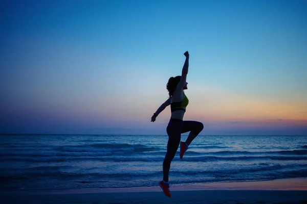 夜のトレーニングで海岸沿いのスポーツスタイルの服で健康なスポーツ女性のシルエット — ストック写真