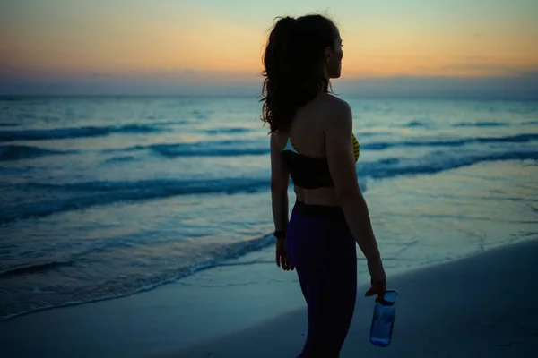 晚上在海滨锻炼后穿着运动服 瓶装水放松的女运动员的轮廓 — 图库照片