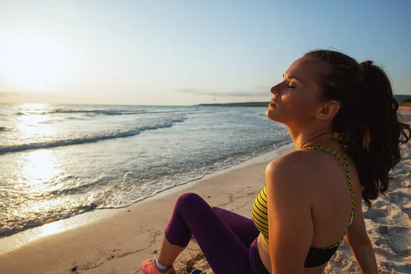 healthy woman in sport style clothes on the ocean coast in the evening relaxing after workout.