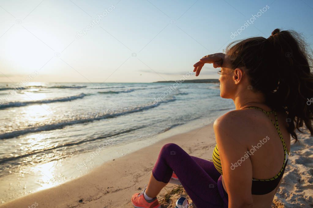 Seen from behind healthy sports woman in sport clothes on the seacoast at sunset looking into the distance.
