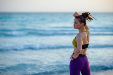Spor kıyafetleri içinde sağlıklı bir kadın akşamları deniz kenarında antrenmandan sonra dinleniyor..