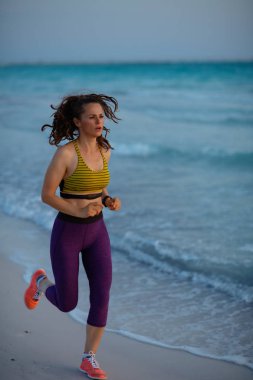 Gün batımında sahilde spor kıyafetlerle koşan sağlıklı kadın portresi..
