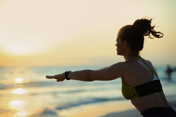 日落时穿着运动服的女运动员在海滨蹲着的轮廓 — 图库照片