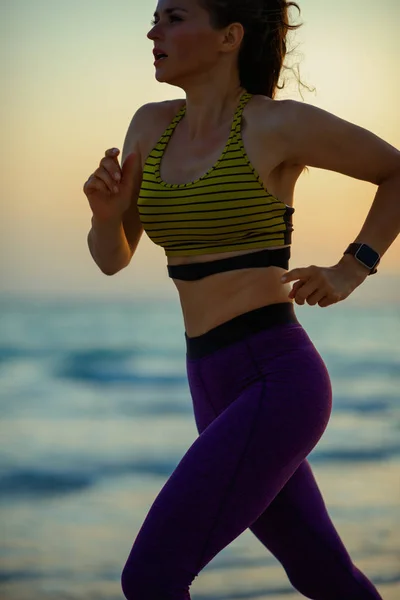 Closeup on healthy sports woman in sport clothes on the ocean shore at sunset running.