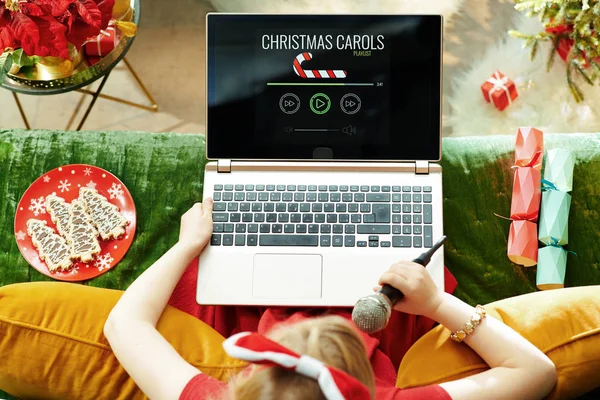 假期季节 圣诞节时 穿着红色衣服的优雅孩子坐在现代客厅的沙发上 一边唱着圣诞颂歌 一边听着笔记本电脑上的歌曲 — 图库照片