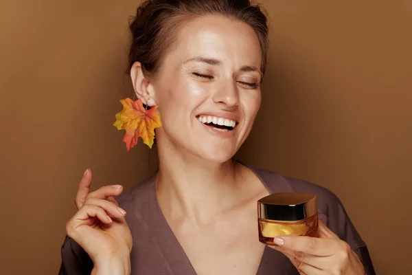 你好秋天 微笑的年轻女子穿着浴袍的肖像 秋叶耳环在米色背景上拿着面部的Créme — 图库照片