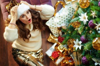 Şok olmuş, uzun sarı saçlı, altın pullu etekli, beyaz kazaklı, hediye kutularının yanındaki Noel ağacının altında fotokopi odasına bakan modern kadın manzarası..