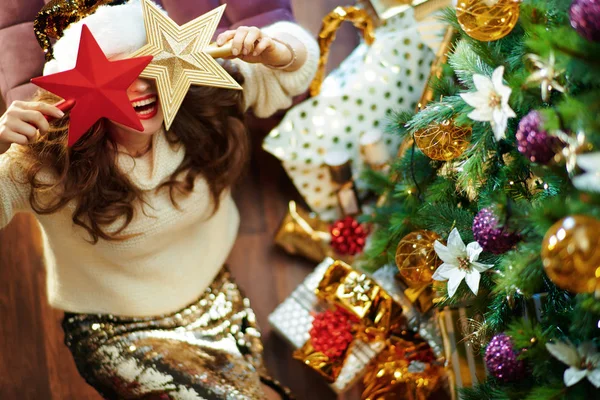 时尚的家庭主妇 一头乌黑的长发 金色的亮片裙 白色的毛衣 挂在装饰过的圣诞树下 — 图库照片
