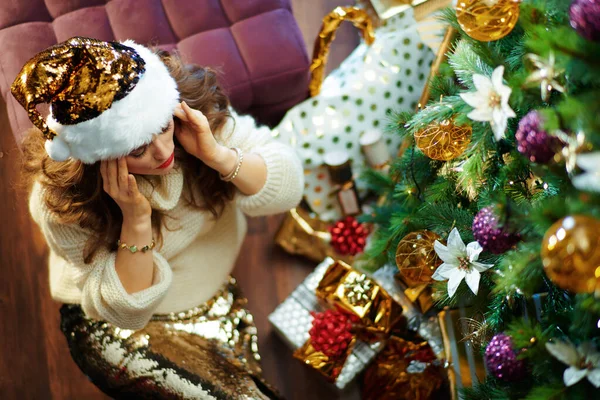 在装饰过的圣诞树下 坐在地板上的盒子旁边 可以看到穿着金色亮片短裙和白色毛衣 留着一头长长的黑发的有压力的时髦女人的上图 — 图库照片