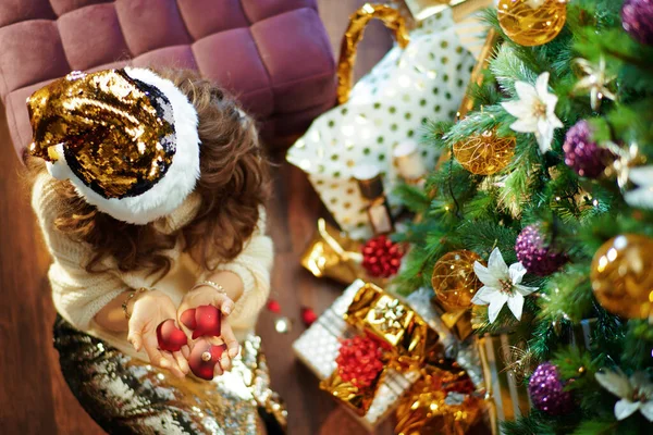 中年时代时髦的家庭主妇 一头长长的黑发 穿着金色亮片裙 白色毛衣 站在装饰过的圣诞树下 靠近装有破碎圣诞球的盒子 — 图库照片