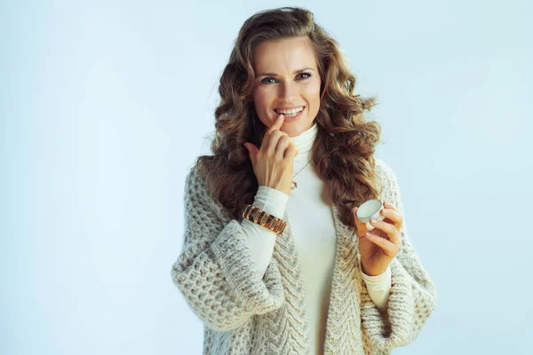 Mujer moderna feliz usando bálsamo labial aislado en invierno azul claro —  Fotos de Stock