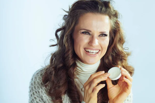 Smiling woman applying lip balm on winter light blue background — ストック写真