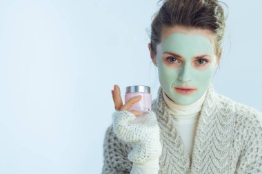 Kozmetik kavanozu tutan yeşil maskeli modern ev kadını.