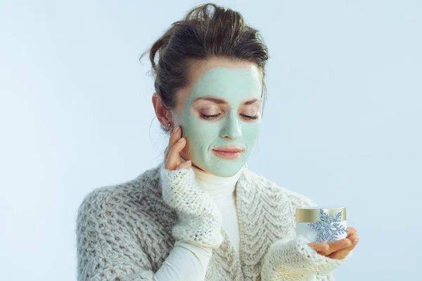 Mujer con máscara facial verde sosteniendo tarro cosmético y copo de nieve — Foto de Stock