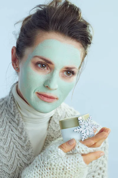 Yüz maskeli ev hanımı elinde kozmetik kavanozu ve kar tanesi tutuyor. — Stok fotoğraf