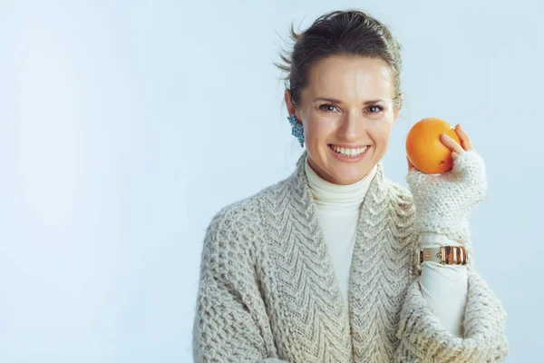 Woman holding orange against winter light blue background — ストック写真