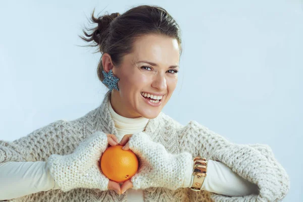 Happy woman showing orange against winter light blue background — Stock Photo, Image