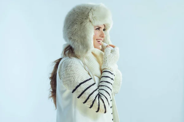 Woman using hygienic lipstick on winter light blue background — Stock Photo, Image