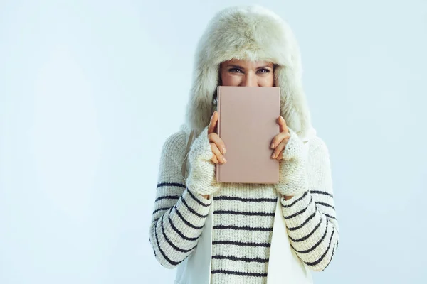 Žena skrývající se za knihou proti zimě světle modré pozadí — Stock fotografie