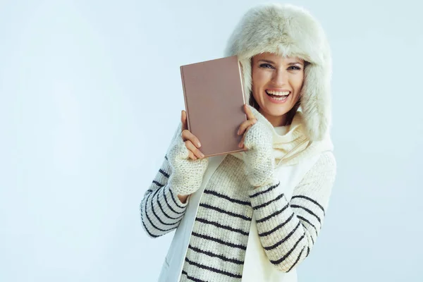 Smiling woman showing book on winter light blue background — ストック写真