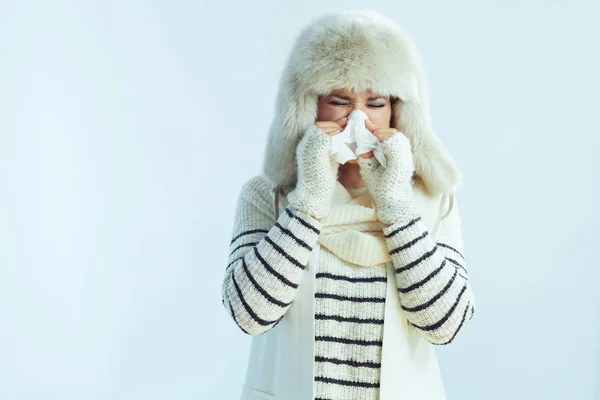 Female with napkin sneezing on winter light blue background — Stock Photo, Image