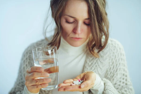 Concerned woman with cup of water holding various pills — Stock Photo, Image
