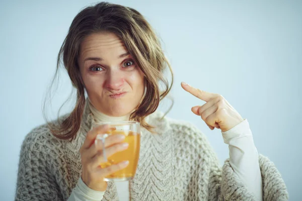 Sad housewife holding cup of tea and pointing on red nose — Stock Photo, Image