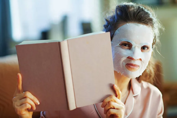 Elegant Woman Pajamas White Sheet Facial Mask Looking Out Book — Stock Photo, Image