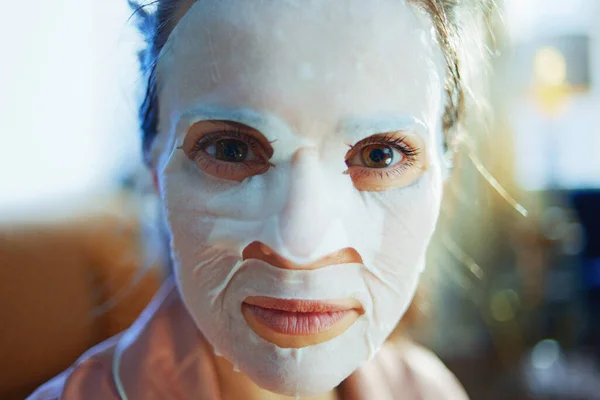 エレガントなの肖像画40歳の女性でパジャマで顔に白いシートマスクで現代の家で晴れた冬の日 — ストック写真