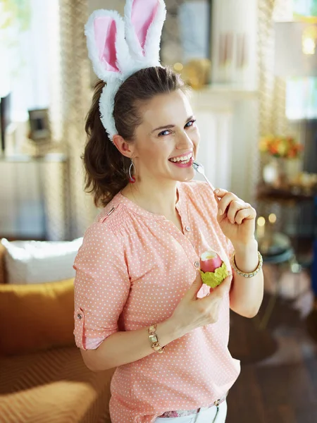 Улыбающаяся Элегантная Женщина Розовой Блузке Пасхальных Кроликах Поедающая Красное Пасхальное — стоковое фото