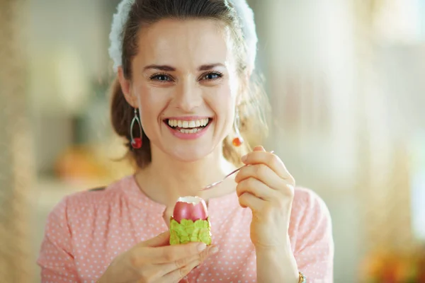 ピンクのブラウスとイースターバニーの耳で現代の女性の笑顔赤いイースターエッグを食べる緑の卵カップにスプーンで現代の家で晴れた春の日 — ストック写真