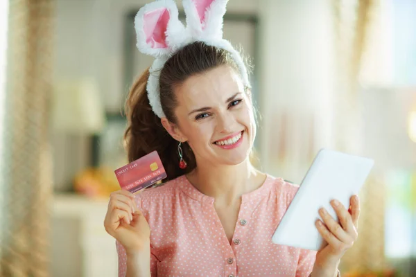 ピンクのブラウスとイースターバニーの耳に幸せな若い女性の肖像画クレジットカードでオンラインで購入します — ストック写真