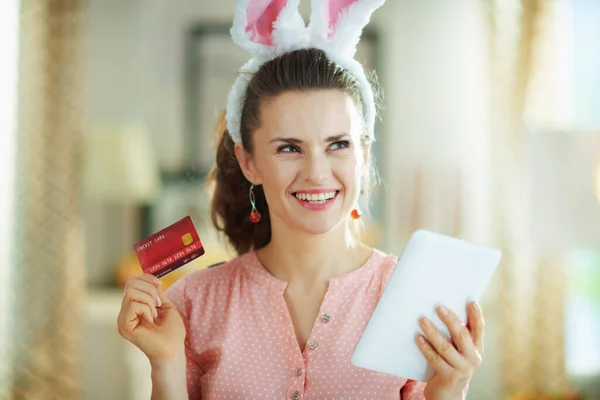 ピンクのブラウスとイースターバニーの耳の中の若い主婦クレジットカードでオンラインで購入します — ストック写真