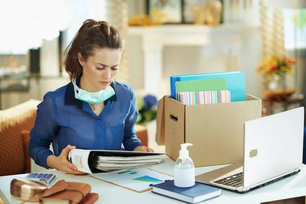 在阳光明媚的现代家庭中 穿着蓝色衬衫 戴着医疗面罩的中年妇女在临时的家庭办公室工作 — 图库照片