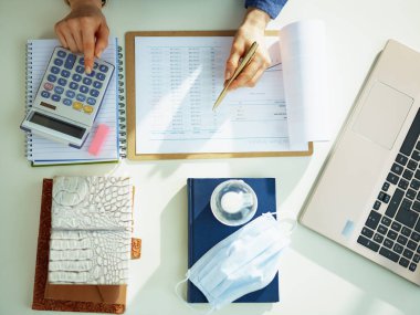 Masada doküman ve hesap makinesiyle çalışan kadınların üst görünümü.