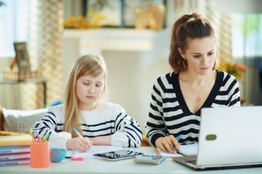 Anne, çocuk güneşli bir günde modern evde ev ödevi yaparken çalışıyor..