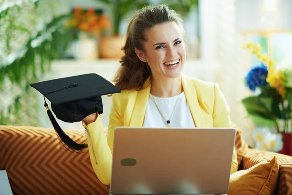 Szczęśliwa Elegancka Uczennica Dżinsach Żółtej Kurtce Laptopem Pokazującym Czapkę Dyplomową — Zdjęcie stockowe