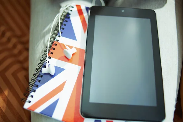 Closeup on tablet PC, headphones and UK flag notebook in the living room in sunny day.