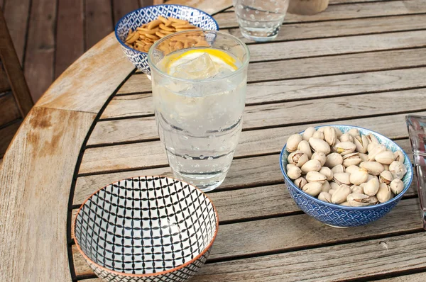 Table with glass of drink and bowls with cocktail nuts — Stock Photo, Image