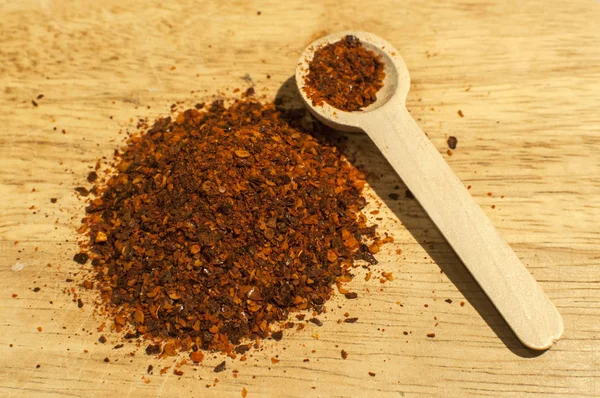 一堆干碎的粗地面红辣椒片和种子香料粉和木制木板上的小木勺特写 — 图库照片