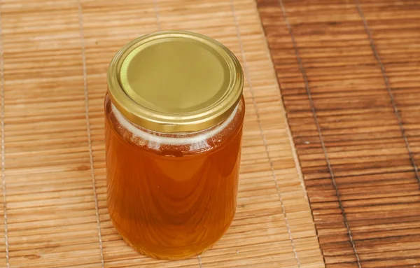 在芦苇垫子上装有蜜蜂蜂蜜特写的玻璃瓶 — 图库照片