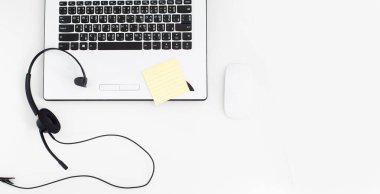 VoIP kulaklık, dizüstü bilgisayarın klavyesine not kağıdı ve kalem. Çağrı merkezi ve müşteri hizmetleri yardım masası için iletişim desteği. Beyaz arka planda izole edilmiş. Üst görünüm düz arkaplan. Metin tasarımı için boşluk